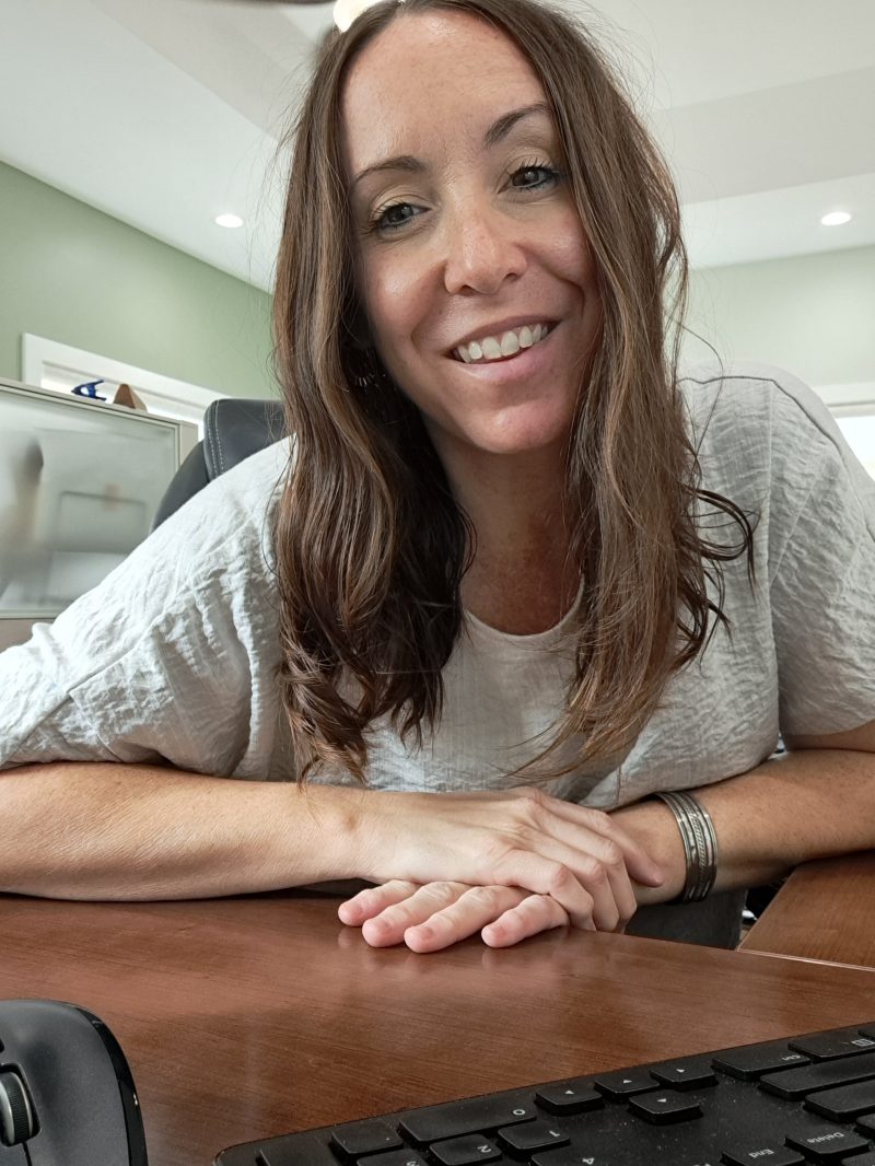 Smiling woman with long hair working at a desk with a keyboard in the foreground.