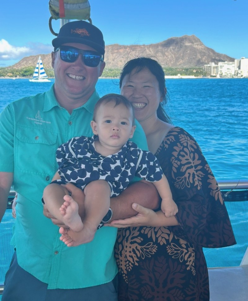 Smiling family with baby on a boat, mountain and ocean in background.