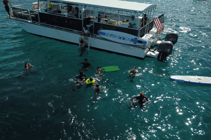 People swimming near a boat with American flag in the ocean under clear skies.