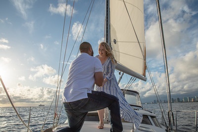 Man proposing to woman on sailboat at sea during sunset.