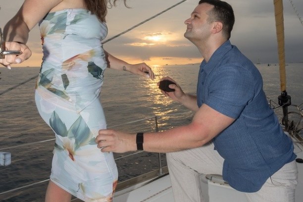 Man proposing on a boat at sunset, kneeling with ring.