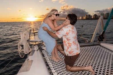 Couple embracing on a boat at sunset with city skyline in background.