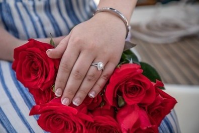 Hand with engagement ring resting on a bouquet of red roses.