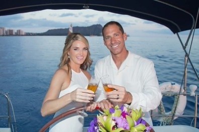 Couple toasting with drinks on a boat, ocean and cityscape in the background.