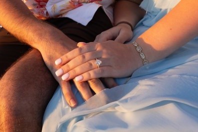 Couple holding hands, woman showing engagement ring.