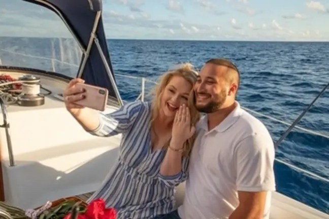 Couple taking a selfie on a sailboat with ocean in the background.